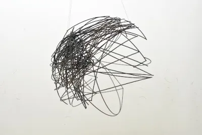 A steel wire sculpture is suspended in a gallery space
