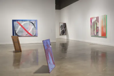 Five paintings are displayed, including 2 on the floor, 2 hung flush against the wall and 1 jutting from the wall.