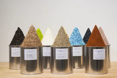 Rows of round tin cans with homemade white labels holding cone shaped mounds of various colored substances and textures