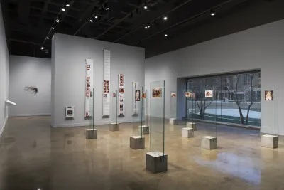 Color photographs mounted on glass panels with concrete bases fill the gallery floor, photo prints on rolls on the back wall.