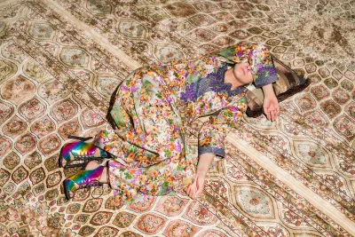 A body is curled up and camoflauging with a colorful carpet.