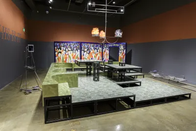 Chandelier with orange glass orbs hangs above a multi-level stage with green banquettes, before a colorful trifold screen.