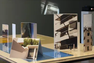 A table top with blue gels under glass and photographs of buildings placed at angles, a slide projection on the back wall