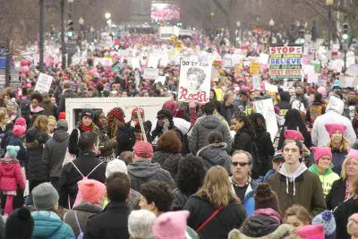 Still showing a massive crowd of protestors wearing pink pussy hats and holding signs, filling the screen.