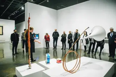 A gallery guide points to sculptures by Tony Conrad and engage a group of gallery visitors.
