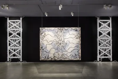 Painting with grayscale vines and the faint shadow of a pelvic bone hangs in front of a black wall from chainlink.