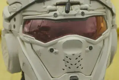 Extreme close up of a person wearing a futuristic storm-trooper-like helmet posing in front of bright yellow vinyl siding.