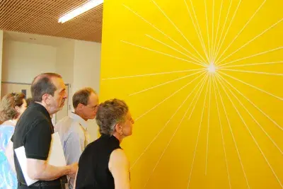 A group of people stare at a bright yellow wall with white lines coming out from the center.