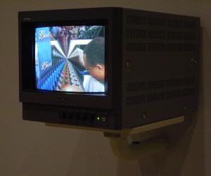 Box television monitor is mounted to the wall; it’s screen shows a colorful image warped and twisted