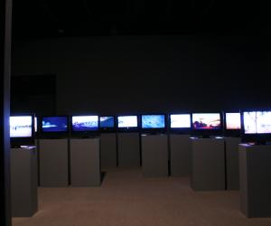 Many screens installed on podiums in a darkened gallery. 