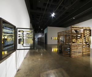 A large gallery with a slatted wood structure like a cabin, and a wall work with mirrored box and a glass window at an angle