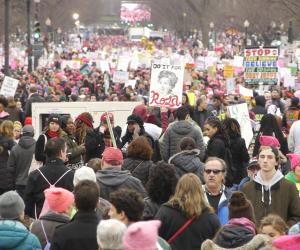 Still showing a massive crowd of protestors wearing pink pussy hats and holding signs, filling the screen.