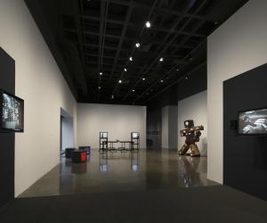 In a long view of a black and white gallery space, several video sculptures are displayed.