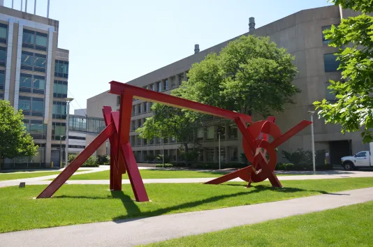 Angled view of a red steel sculpture on a green lawn.