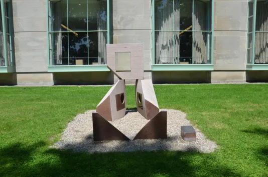 Granite sculpture in the center on green grass with a building in the background.