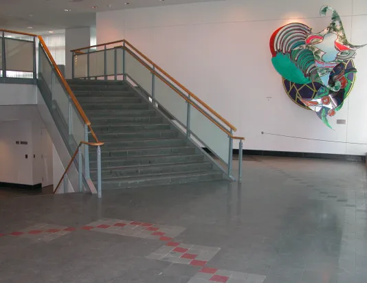 Installation view of a grey floor with red accents featuring a staircase and sculpture in the background.