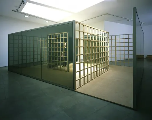 Installation view of a sculpture that resembles a building with lots of mirrors and a grid running along the side.