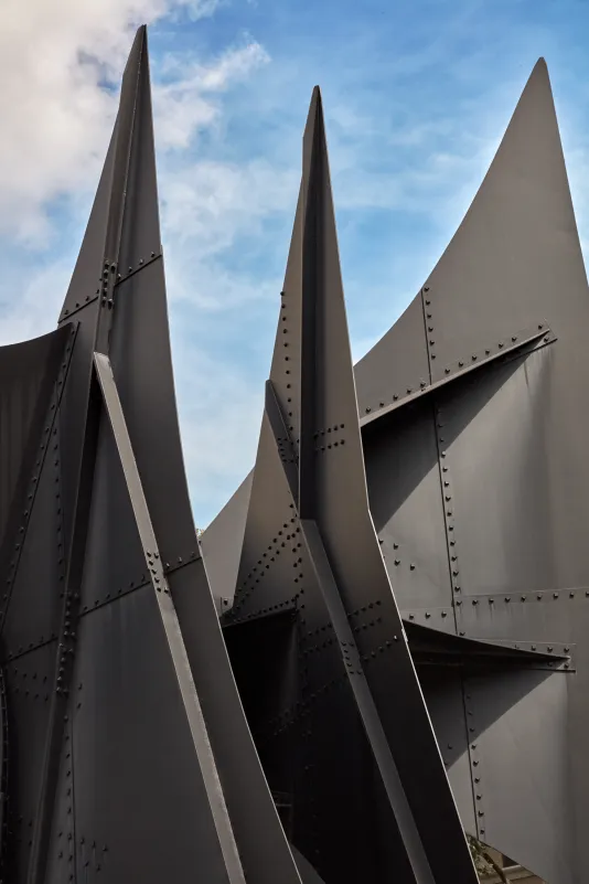 Detail of large steel sculpture with pointed edges. A blue sky is peeking through in the background.
