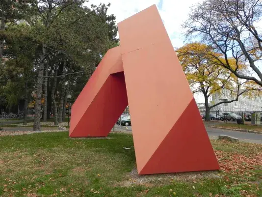 Red steel sculpture resembling a rectangular prism has been bent into the confines of a larger triangular pyramid