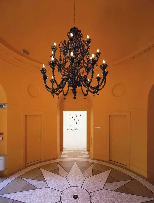 Black chandelier hangs in a yellow domed room with a star shape on the tile floor.