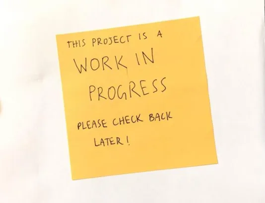 White postcard with a yellow sticky note that reads "this project is a work in progress please check back later!