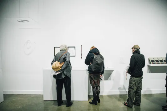 Three visitors look at art in a gallery with their backs facing the camera.