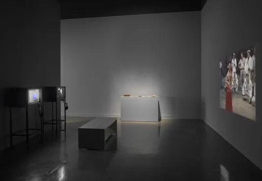  gallery at the MIT List Visual Arts Center includes two television sets, a bench, a vitrine, and a projection by Leslie Thornton.