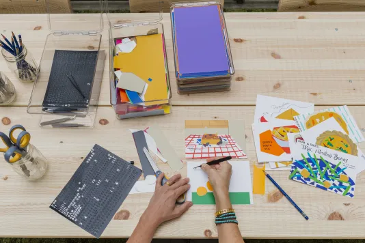 Overhead shot of someone's hands working at a wooden table with art supplies