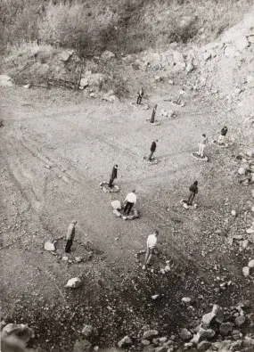 Black and white photo from above of people standing in circles of rocks  in an area of dirt