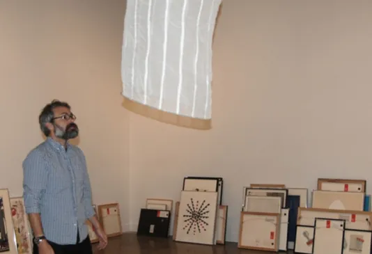 A man stands in a gallery with framed art lining the wall to his left.