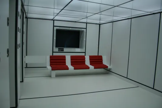 Futuristic red chairs built into a white room with black panels running along the wall and floor.