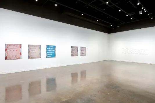 Installation view featuring five colored inkjet prints on vinyl on the left wall and a mural of warped text on the far-right wall. 