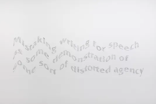 White gallery wall with a mural that has three lines of gray, wavy looking text.