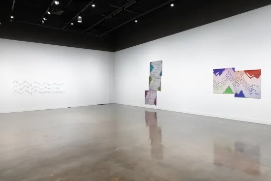  Installation view featuring a set of three inkjet prints on vinyl on a wall next to two prints side by side and a gray text mural on the far-left wall. 