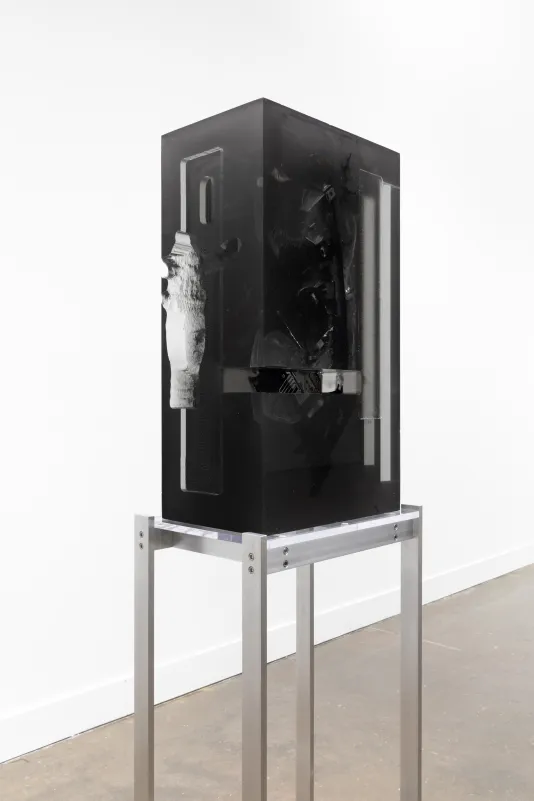 Installation view of a black headlight encased in a block of dark resin on a tall metal stand. 
