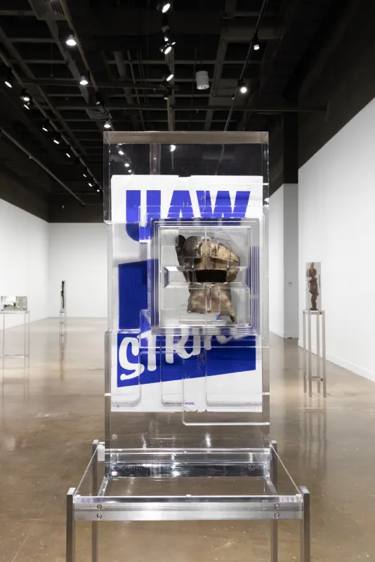 Installation view of a work glove in front of a blue and white poster that reads “UAW” on strike encased in a block of resin.