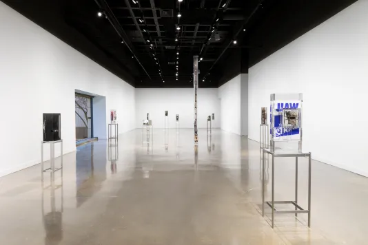 Exhibition view featuring 10 sculptures of varying sizes with objects inside of blocks of clear resin spread throughout the gallery. Each sculpture is on a tall metal stand.