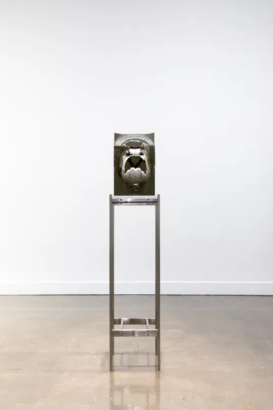 Installation view of a white and black helmet encased in a rectangular block of resin on a tall metal stand. 