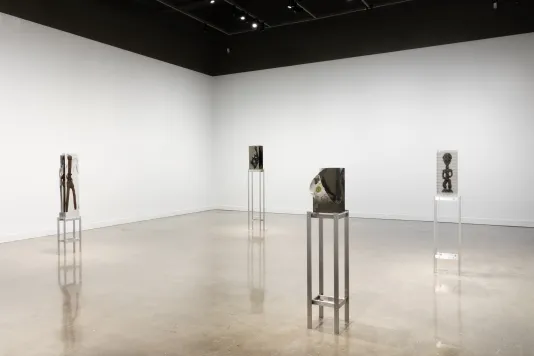 Exhibition view featuring around 4 sculptures of varying sizes with objects inside of blocks of clear resin spread throughout the gallery. Each sculpture is on a tall metal stand.