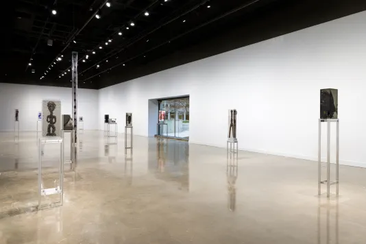 Exhibition view featuring 12 sculptures of varying sizes with objects inside of blocks of clear resin spread throughout the gallery. Each sculpture is on a tall metal stand.