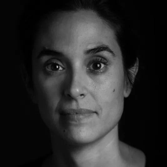 Black and white headshot of a woman with dark hair, pulled back. She wears a black v-neck shirt