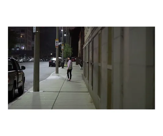 Image of a woman walking down an empty sidewalk at night looking back towards the camera.