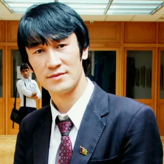 Sorosh poses, wearing a dark suit jacket overtop white button &amp; patterned tie. He has straight, dark hair that covers his forehead