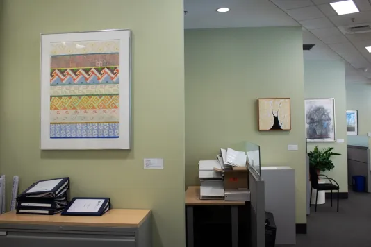 Four office walls on the left each with a framed artwork on the wall leading down a hallway. 