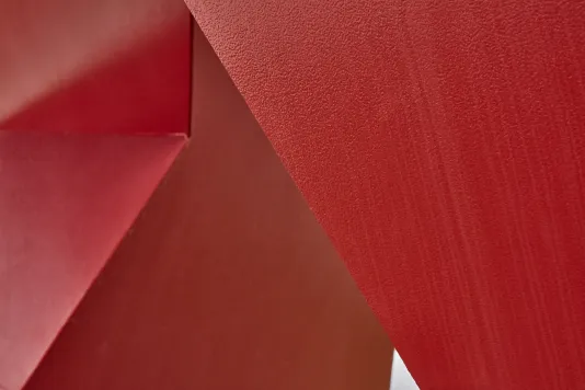 Detailed view of a red painted steel sculpture with a smooth surface and hard edges. 