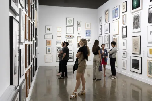 Installation view with framed artworks and a group of people gathered in the center.