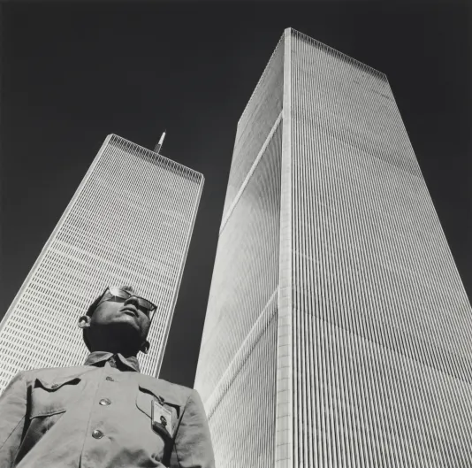 Black and white photograph from below of a man next two two tall skyscrapers.