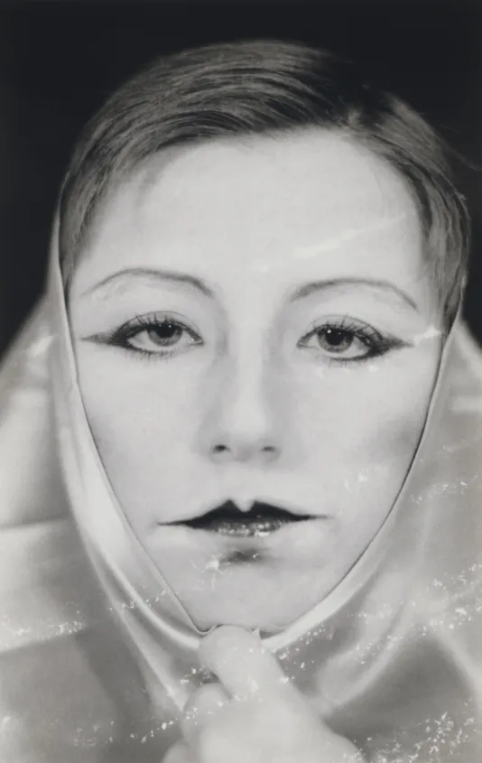 Black and white photograph of a woman looking right at the camera with bold lipstick on and a scarf around her head.
