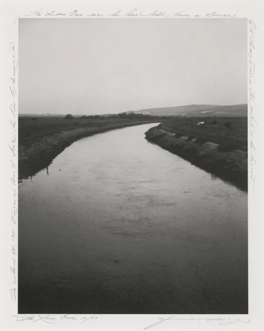 Black and white photograph of a river with marsh on each side and a clear sky.