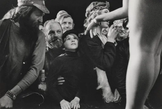 Black and white phot collage with a child in the center and other people looking at him and a hand on the right reaching out towards him.